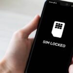 「SIM LOCKED」と表示されたスマートフォン画面を手に持ち、SIMロック状態を示している様子
