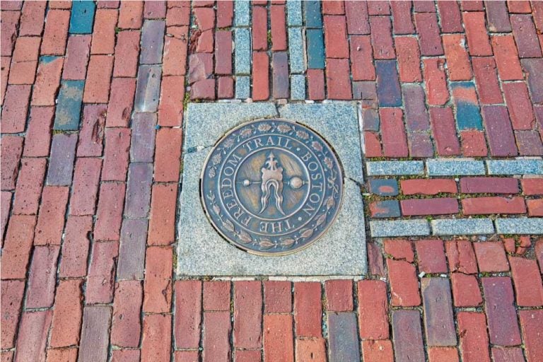 ボストンのフリーダム・トレイルの道標を示す金属製の丸いプレート。赤レンガの歩道に埋め込まれており、歴史的な街並みを辿るための重要な目印となっている。