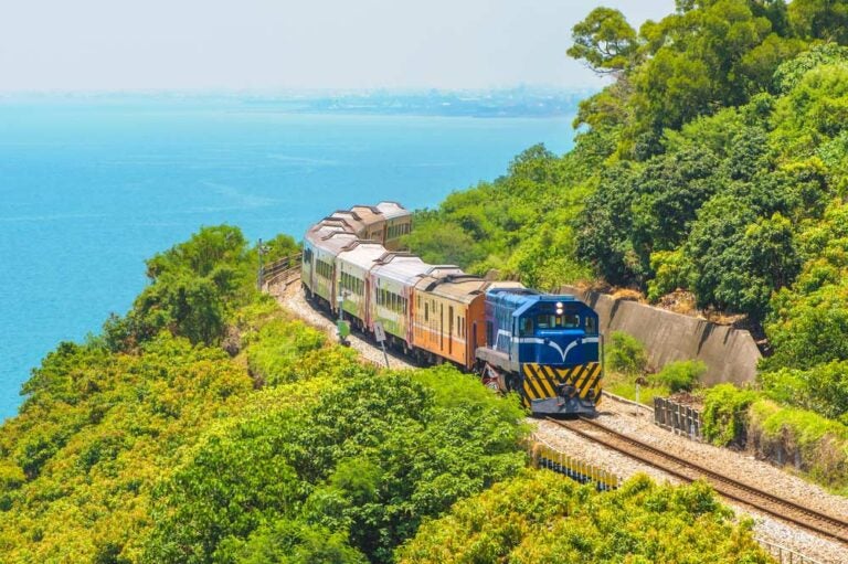 青い海と緑の山に囲まれた沿岸を走るカラフルな台湾の列車。台湾旅行や鉄道の旅、絶景ルートの紹介にぴったりのイメージ。