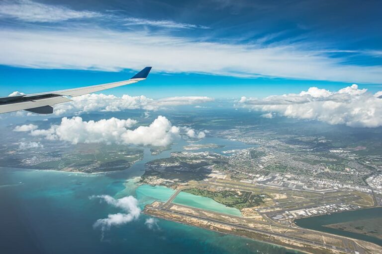 飛行機の翼の向こうに広がるハワイ・オアフ島と海の空撮風景
