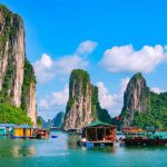 ベトナムのハロン湾の風景。石灰岩の奇岩が青空とエメラルドグリーンの海に映え、カラフルな家やボートが浮かぶ平和な水上集落の様子。