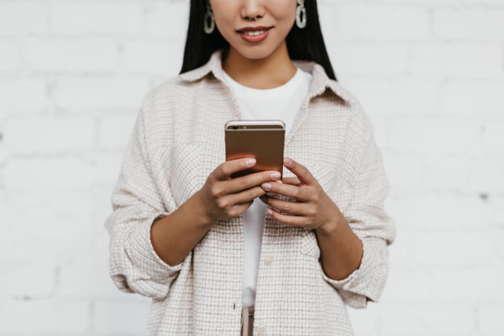 白い背景の前でスマートフォンを操作している女性。