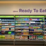 韓国のコンビニにある「Ready To Eat」コーナーの棚。ジュースや牛乳、ヨーグルトドリンクなどの飲料と、サンドイッチやおにぎりなどの軽食が並んでいる。上部には韓国語で「간편식사（簡便食事）」と書かれている。