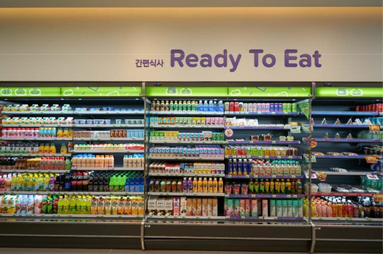 韓国のコンビニにある「Ready To Eat」コーナーの棚。ジュースや牛乳、ヨーグルトドリンクなどの飲料と、サンドイッチやおにぎりなどの軽食が並んでいる。上部には韓国語で「간편식사（簡便食事）」と書かれている。