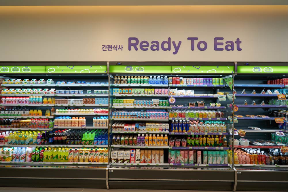 韓国のコンビニにある「Ready To Eat」コーナーの棚。ジュースや牛乳、ヨーグルトドリンクなどの飲料と、サンドイッチやおにぎりなどの軽食が並んでいる。上部には韓国語で「간편식사（簡便食事）」と書かれている。