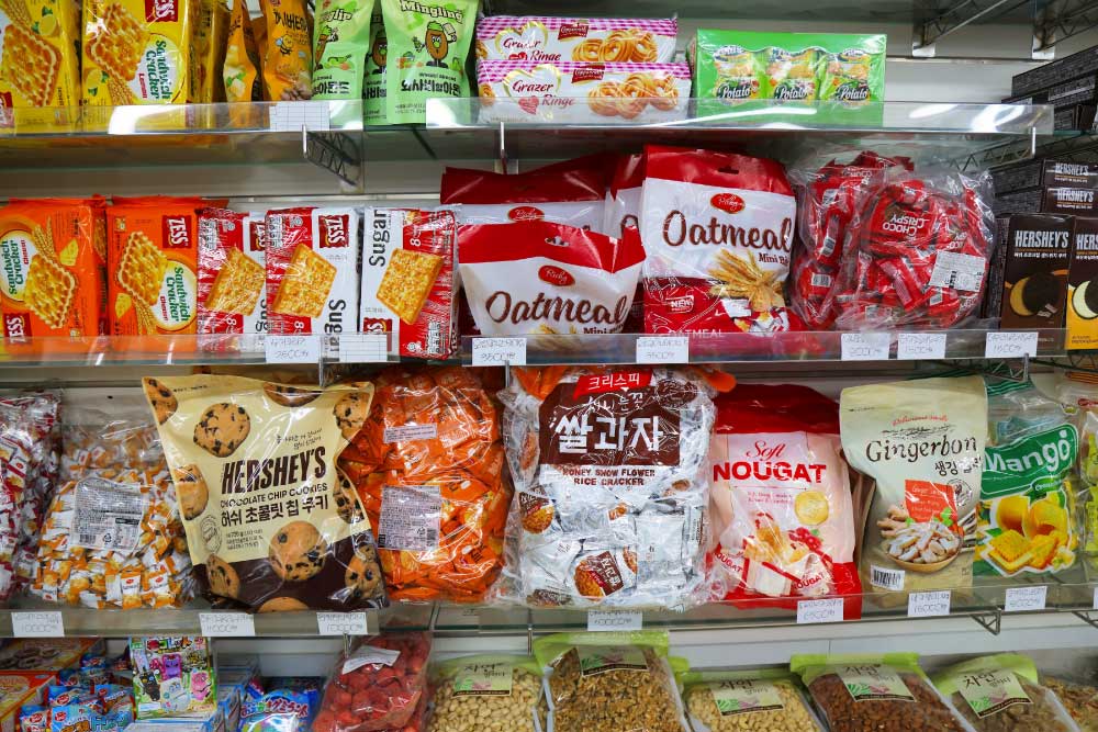 韓国のコンビニに並ぶお菓子の棚。クラッカー、クッキー、チョコレート、ヌガー、伝統的な米菓子（쌀과자）など、さまざまなお菓子が陳列されている。