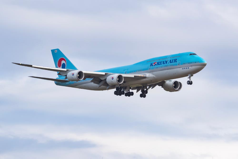 青空の下で着陸態勢に入っている大韓航空の飛行機。飛行機の機体は明るい青色で、「Korean Air」のロゴが見える。