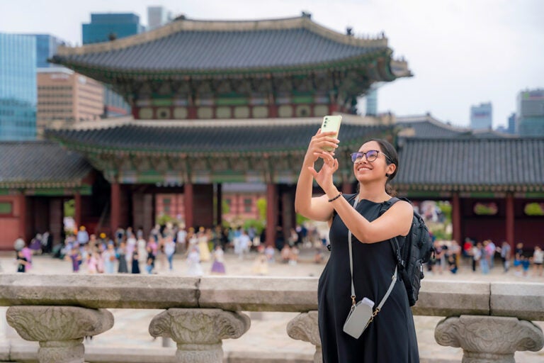 景福宮をバックにスマホで写真を撮る韓国旅行中の女性