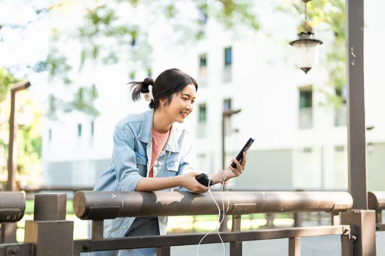 
韓国旅行中にモバイルバッテリーでスマホを充電しながら笑顔で操作する女性