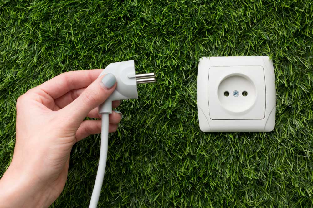 芝生の上に設置された白い電源コンセントと、プラグを持つ手。