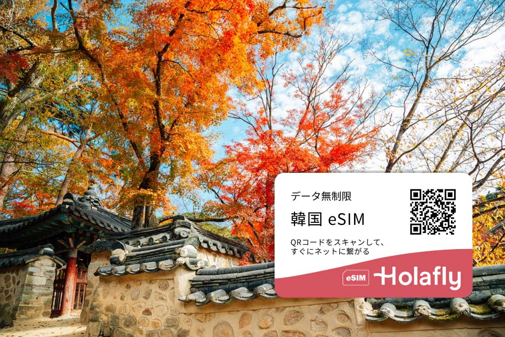 韓国の秋の紅葉が広がる伝統的な建築の風景と、HolaflyのeSIM広告。韓国旅行向けのデータ無制限eSIMのプロモーション画像で、QRコードをスキャンしてすぐにネット接続が可能。