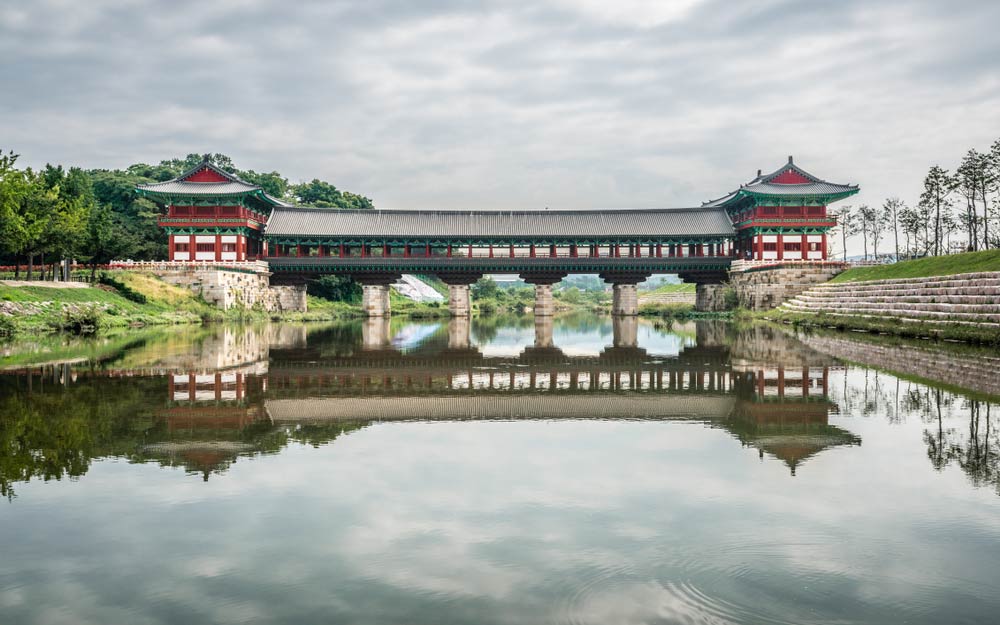 韓国・慶州の月精橋（ウォルジョンギョ）。朝の静かな時間に、伝統的な木造の橋が川面に映り、美しいシンメトリーを作り出している。