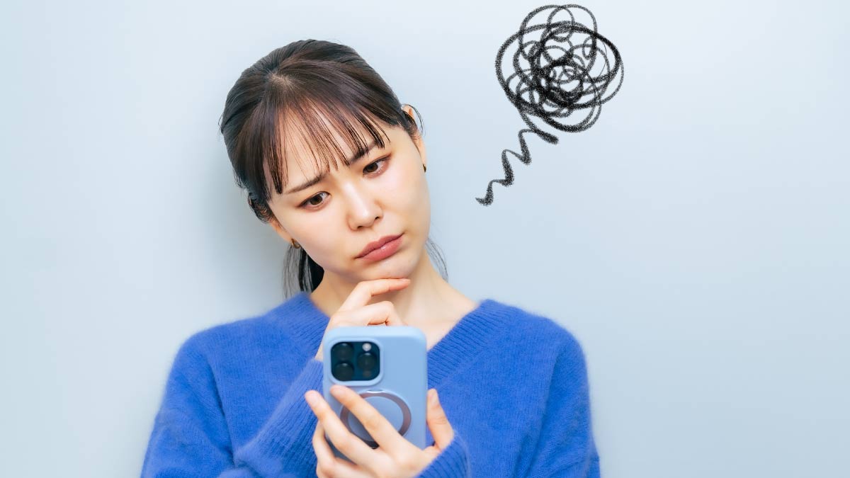 青いセーターを着た女性がスマートフォンを見て困惑した表情をしている様子。頭の上に混乱を表す黒い渦巻きが描かれている。
