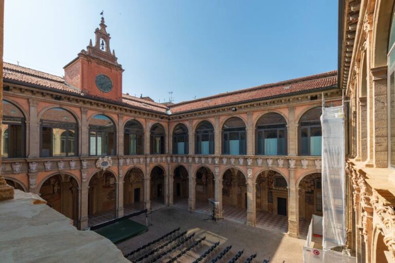 イタリア・ボローニャ大学の歴史ある中庭(アルキジンナジオ)。ルネサンス様式の建築が美しく、アーチに囲まれた中庭にはイベント用の椅子が並べられている。