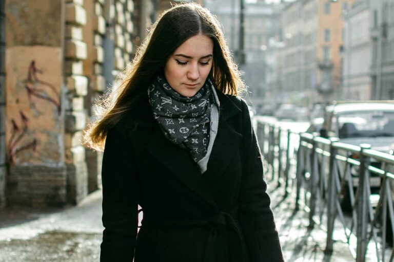 冬用のコートとマフラーを身につけた女性がイタリアの街を背景に佇んでいる写真