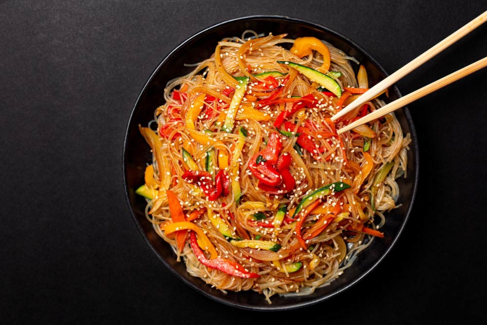 韓国の人気麺料理「ビビンタンミョン」。春雨のような透明な麺をピリ辛のコチュジャンソースで和え、シャキシャキの野菜と胡麻をトッピング。