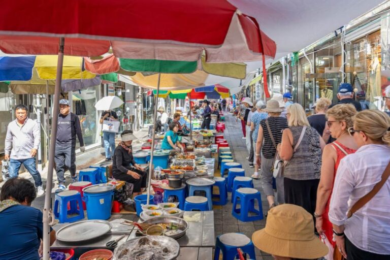 韓国・釜山の国際市場にある屋台街の風景。カラフルなパラソルの下に並ぶ屋台では、地元の名物料理が提供され、観光客や地元の人々で賑わっている。