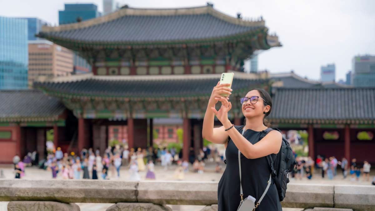 ソウルの景福宮(キョンボックン)前で自撮りをする女性観光客。伝統的な建築と背景に広がる現代的な高層ビルが対照的。