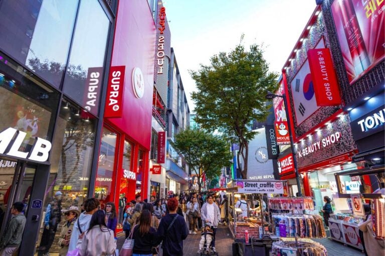 韓国・ソウルの明洞（Myeongdong）ショッピングストリートの活気ある風景。K-ビューティーショップや人気ブランドの店舗が立ち並び、多くの観光客や買い物客で賑わっている。