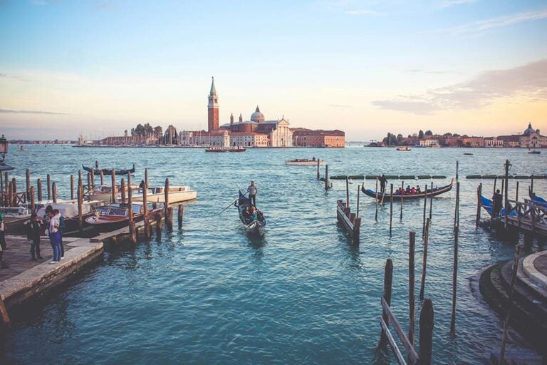 ベネチアの運河で男性が観光客のカップルを乗せて船を漕いでいる写真