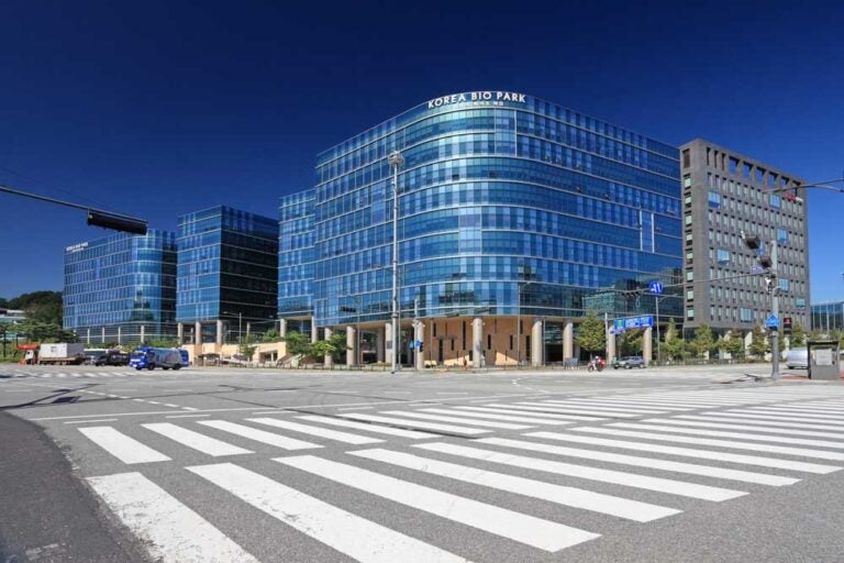 青空の下に広がる、韓国・清州のバイオ産業拠点「Korea Bio Park」のオフィスビル群。モダンなガラス張りの建物が並び、最先端の研究と開発が行われている。