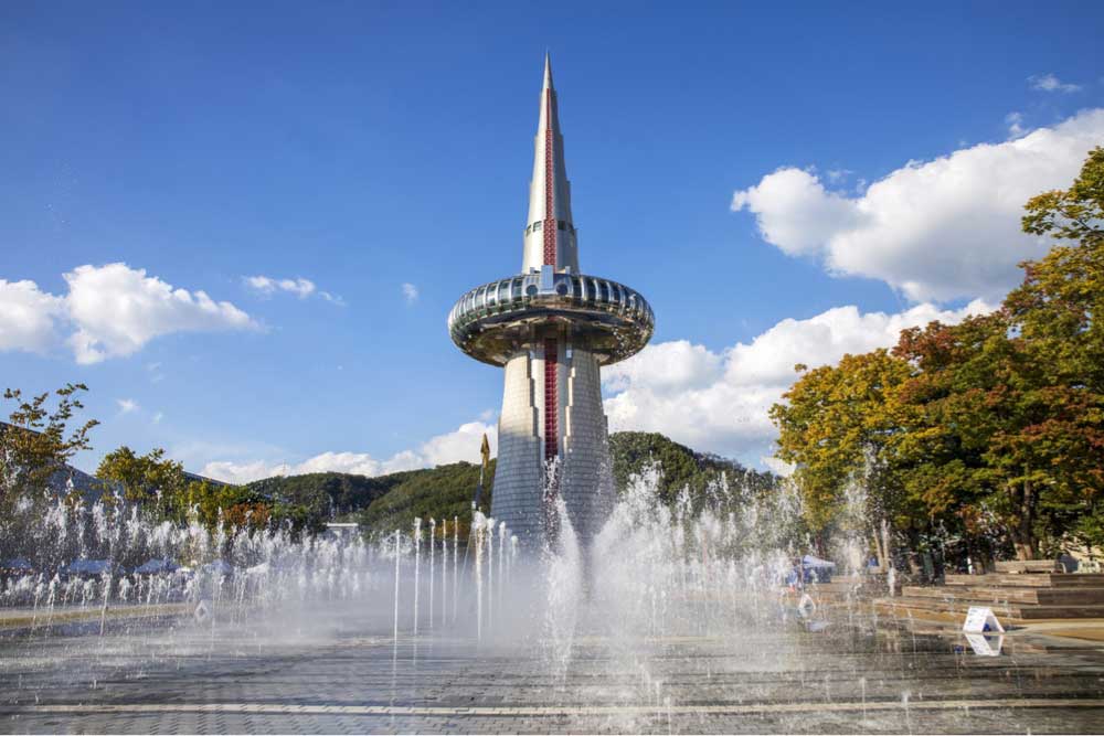 韓国・大田(テジョン)にあるハンビッタワー。青空の下で噴水が躍動し、近未来的なデザインの展望タワーが目を引く風景。エキスポ科学公園内のランドマークとして知られる。