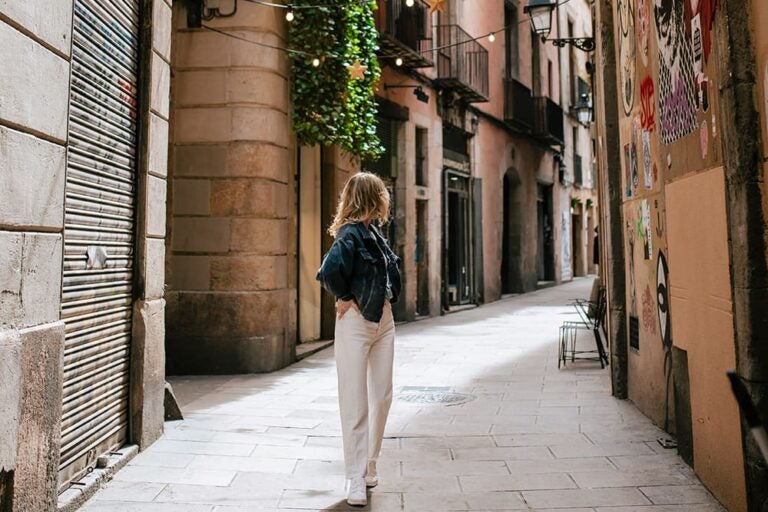 バルセロナの街を散策している女性の写真。デニムジャケットに白い長ズボンを履いている。
