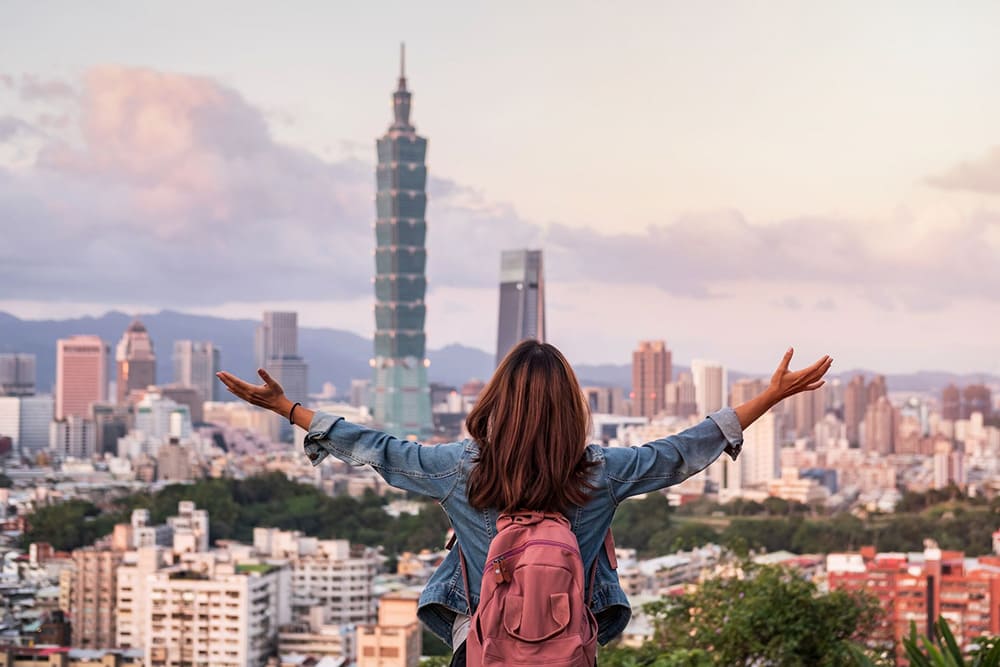 台北101を望む展望台で両手を広げる女性旅行者の後ろ姿。週末の短期旅行にぴったりな台湾・台北の街並みを象徴する写真