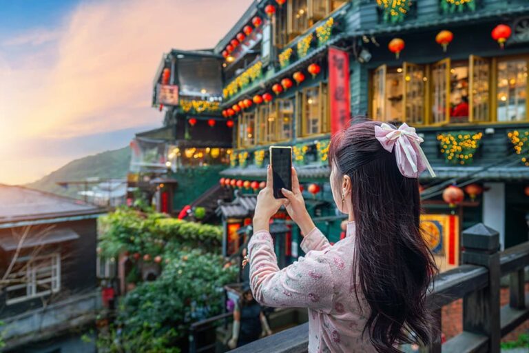 夕暮れの九份老街で赤い提灯を背景にスマートフォンで撮影する女性