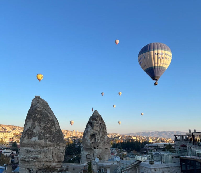 トルコ・カッパドキアの早朝、青空に舞い上がる気球と独特な奇岩群。