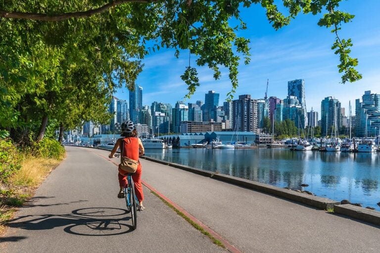 スタンレーパークのシーウォールを自転車で走りながらバンクーバーの街並みとマリーナを眺める女性