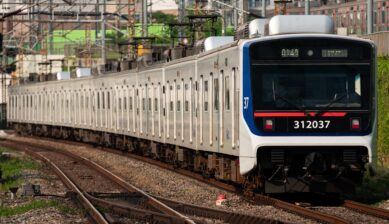 韓国・KORAIL（コレール）の通勤電車が線路を走行している様子。青と赤のラインが特徴的な車両で、都市部の防音壁に囲まれた区間を進む姿が写されている。