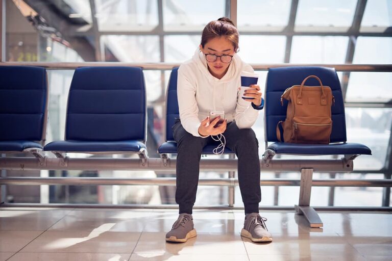 飲み物を持ちスマホを見ながら移動の合間を過ごす旅行者