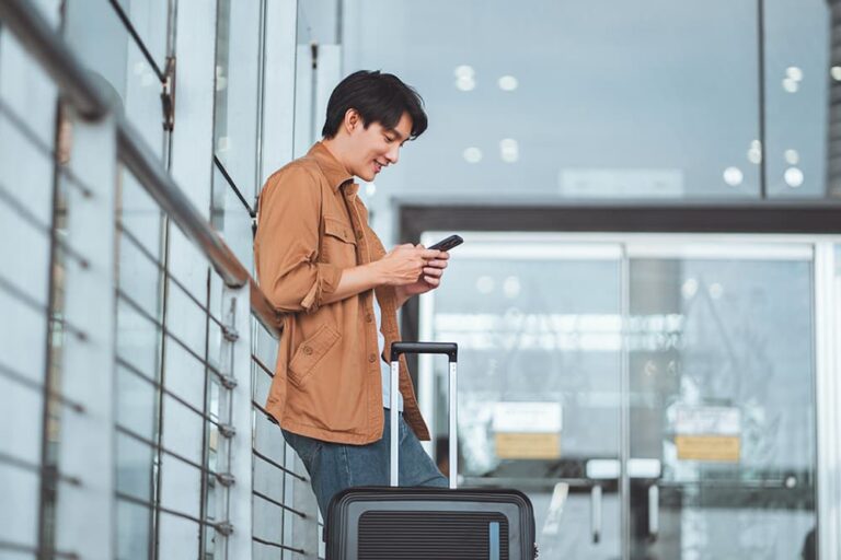 スーツケースを持ち到着後にスマホで通信を使う旅行者