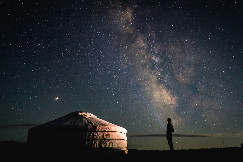 モンゴルの草原でゲルに泊まりながら星空を眺める人の夜景