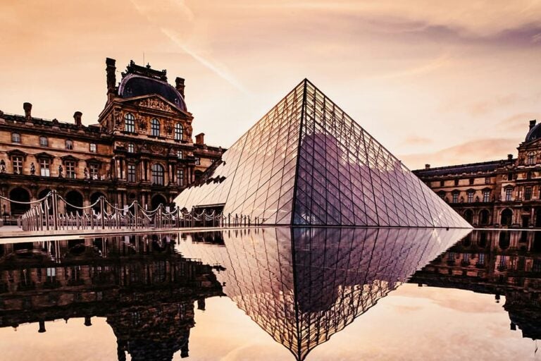 夕暮れ時のルーブル美術館とガラスのピラミッドが水面に映る幻想的な風景を紹介する写真。歴史とモダンが融合するパリを象徴