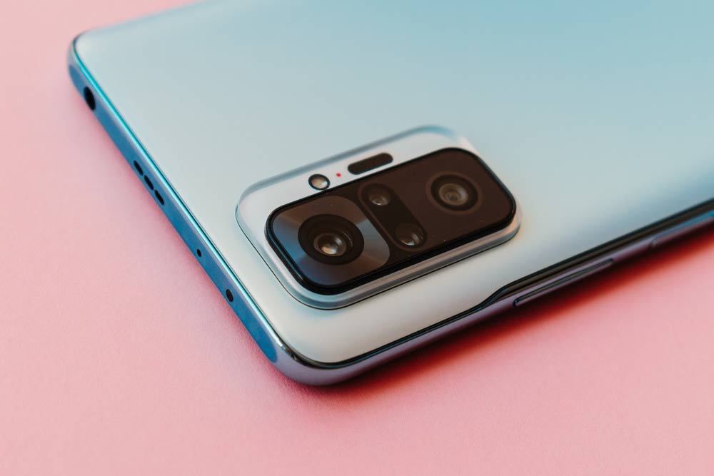 ピンクの背景に置かれたスマートフォンの背面カメラ部分。洗練されたデザインと先進的なカメラユニットが印象的。