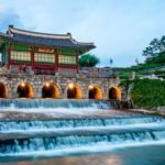 韓国・水原の世界遺産「華城」にある華虹門。石造のアーチとその下を流れる滝のような水路が印象的で、伝統建築と自然が美しく調和している夕暮れの風景。