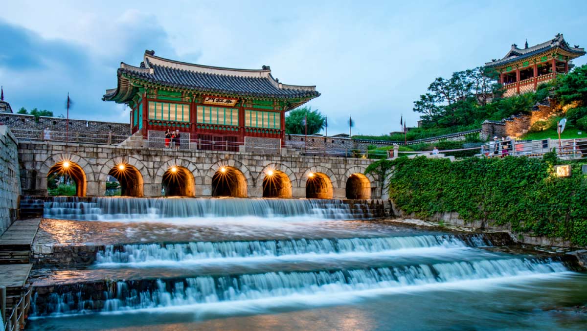 韓国・水原の世界遺産「華城」にある華虹門。石造のアーチとその下を流れる滝のような水路が印象的で、伝統建築と自然が美しく調和している夕暮れの風景。