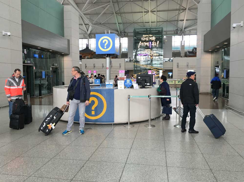 韓国・仁川国際空港の案内カウンター前に立つ旅行者たちの様子。