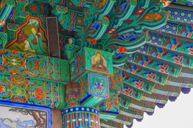 韓国の伝統的な寺院の軒下装飾「丹青（ダンチョン）」。極彩色で描かれた仏像や僧侶の絵が柱や梁に施されており、精緻な模様が寺院建築の美しさを引き立てている。