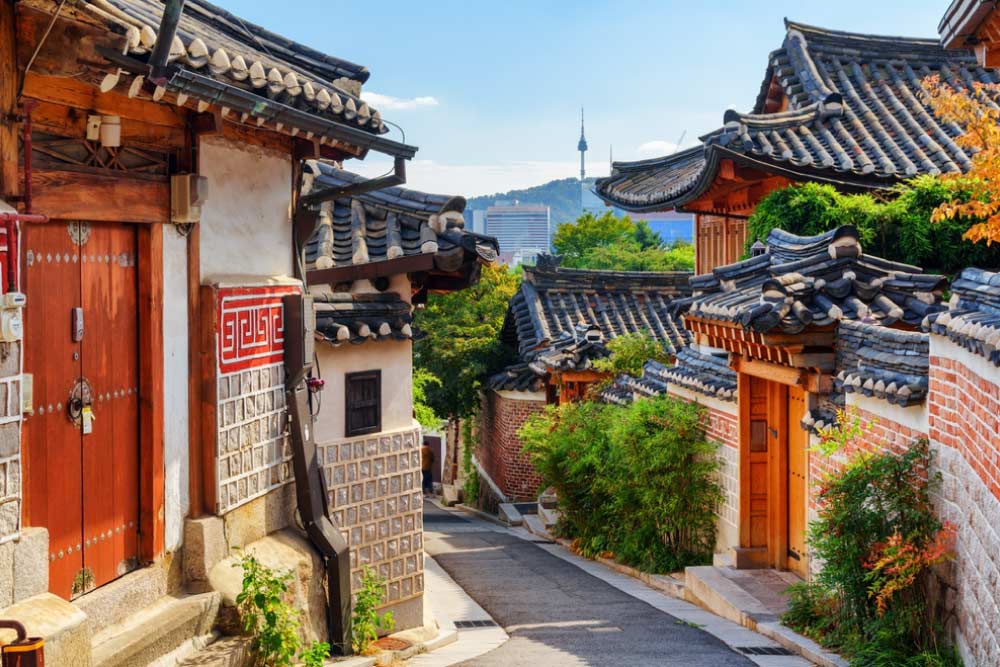 韓国・ソウルの北村韓屋村の伝統的な家屋が並ぶ石畳の路地。背景には南山ソウルタワーが見え、歴史と現代が調和する美しい景観が広がる
