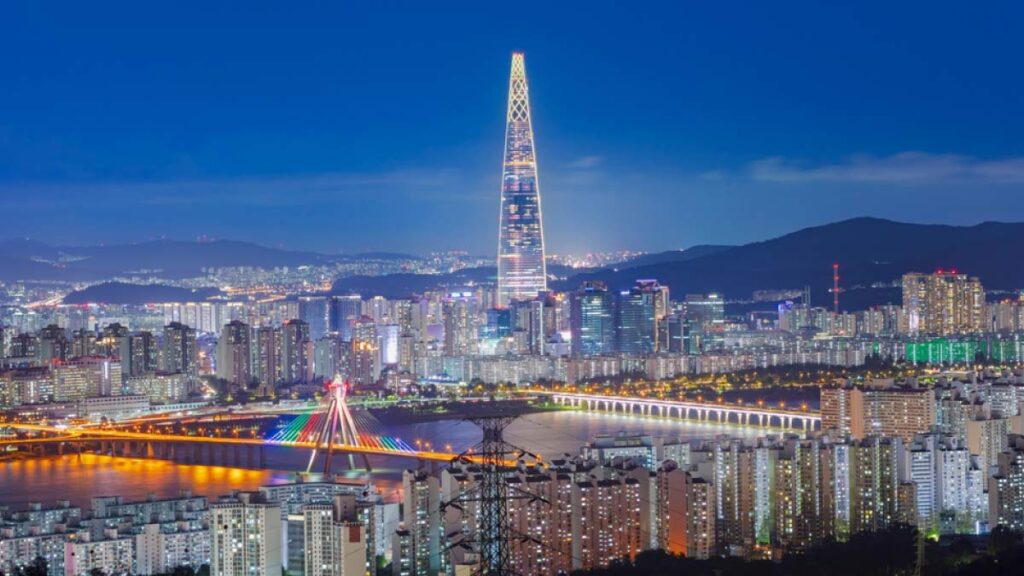 韓国・ソウルのロッテワールドタワーが夜空に輝く風景。漢江にかかるカラフルな橋と高層ビル群が、ダイナミックな都市の夜を演出している。