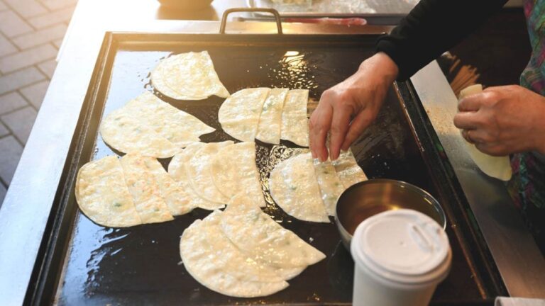 韓国の屋台でナプチャクマンドゥ(平たい餃子)を鉄板で焼く様子。手作業で丁寧に焼かれる薄い餃子が食欲をそそる。