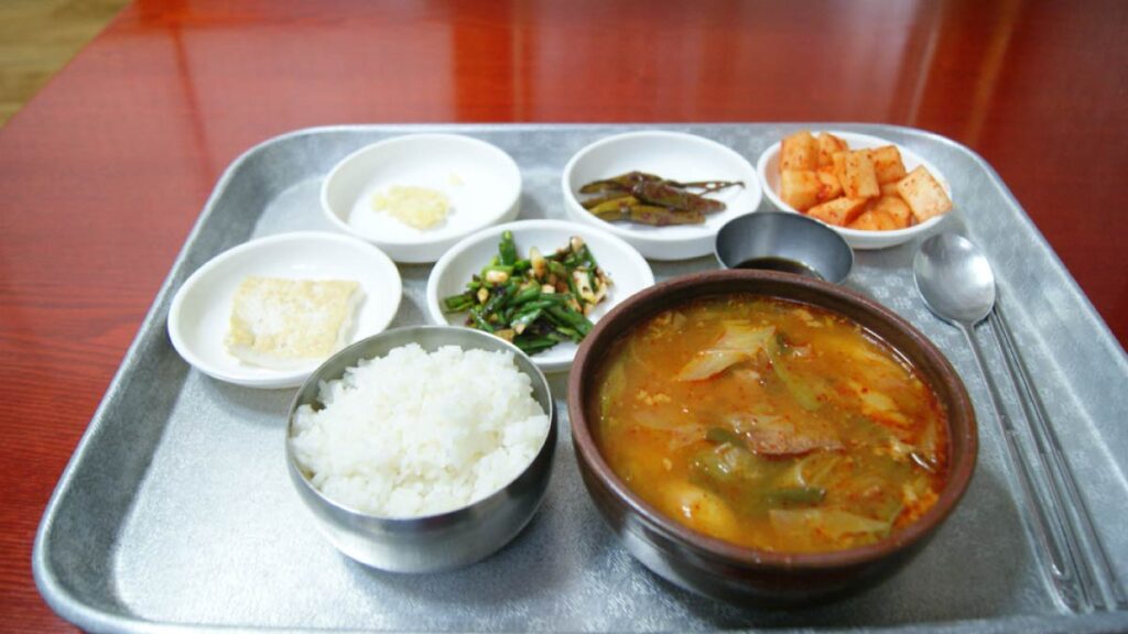 韓国の伝統的な定食スタイル。ごはん、テンジャンチゲ、小皿のキムチやナムルなどが銀色のトレーに並び、素朴で家庭的な韓国料理が味わえる。