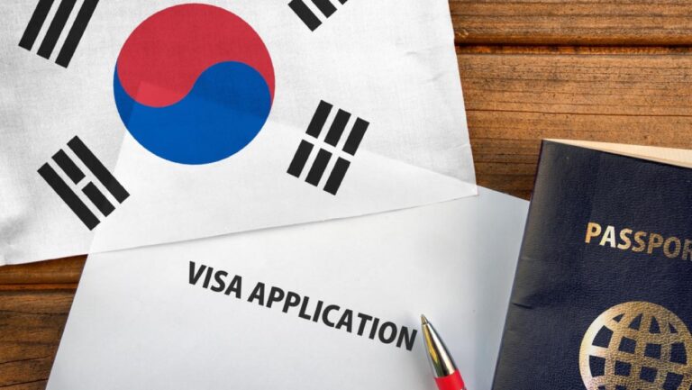韓国の国旗と一緒に、ビザ申請書類とパスポート、赤いペンが木製のテーブルの上に置かれている。韓国への入国に必要なビザ手続きや旅行準備をイメージさせる構図。