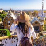 スペイン・バルセロナのグエル公園で景色を眺める旅行者。ガウディ建築とカラフルなモザイクが広がる観光名所の風景。