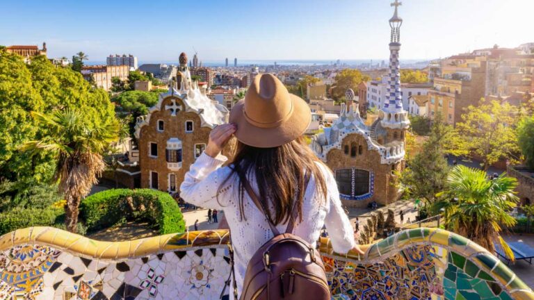 スペイン・バルセロナのグエル公園で景色を眺める旅行者。ガウディ建築とカラフルなモザイクが広がる観光名所の風景。
