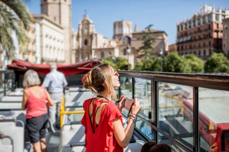 スペイン・バレンシアの観光バスで市内を巡る旅行者。歴史的な街並みを眺めながら、カメラを手に旅の思い出を記録する女性の姿。