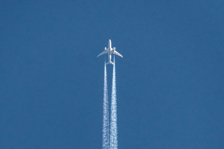 青空を飛行する旅客機と飛行機雲を捉えた写真。8月の海外旅行をおトクに楽しむためのヒントを紹介するセクションのイメージビジュアルに最適